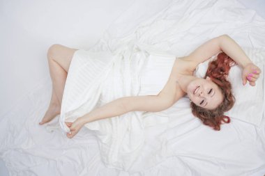 güzel genç kız beyaz bir yatakta yatıyor ve sabah zevk. büyüleyici beyaz kadın mutlu ve rahatlatıcı. uykulu ve tembel kişi yavaş yavaş tek başına poz.