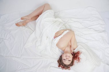 güzel genç kız beyaz bir yatakta yatıyor ve sabah zevk. büyüleyici beyaz kadın mutlu ve rahatlatıcı. uykulu ve tembel kişi yavaş yavaş tek başına poz.