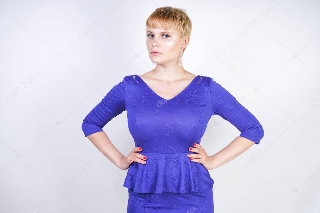 beautiful caucasian girl with short hair and plus size body dressed in blue medium length dress in business style with peplum at the waist. pretty curvy woman standing on white studio background.