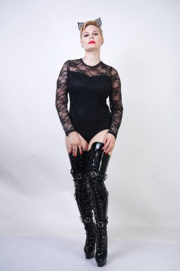 beyaz stüdyo arka plan üzerinde poz kısa sarı saçlı güzel artı boyutu genç kadın. siyah dantel bodysuit sıcak tombul moda kız ve patent deri uyluk yüksek çizmeler kedi kadın tek başına ayakta.
