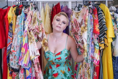 mağazada yürüyen şık bir elbise güzel buxom kız ve tek başına Alışveriş Merkezi'nde askıları trendy kostümleri bakarak, yeni giysiler seçer. sarışın artı moda mağazasında boyutu kadın.