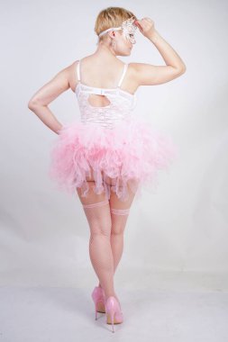 beyaz dantel korse ve tutu etek stüdyo arka planda tek başına ayakta güzel artı boyutu eğlenceli yetişkin kız. pembe elbiseli sevimli sarışın tombul kadın bir bebek kılığında.