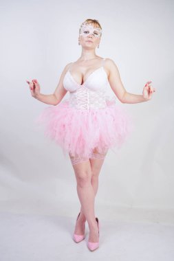 beyaz dantel korse ve tutu etek stüdyo arka planda tek başına ayakta güzel artı boyutu eğlenceli yetişkin kız. pembe elbiseli sevimli sarışın tombul kadın bir bebek kılığında.