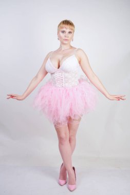 beyaz dantel korse ve tutu etek stüdyo arka planda tek başına ayakta güzel artı boyutu eğlenceli yetişkin kız. pembe elbiseli sevimli sarışın tombul kadın bir bebek kılığında.