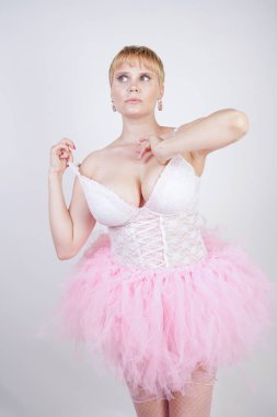 beyaz dantel korse ve tutu etek stüdyo arka planda tek başına ayakta güzel artı boyutu eğlenceli yetişkin kız. pembe elbiseli sevimli sarışın tombul kadın bir bebek kılığında.