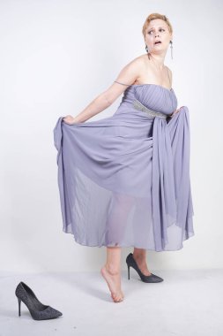 büyüleyici artı gri elbise elbiseli genç kadın Studio beyaz arka planda terlik kaybetti. gece kıyafetleri ve yüksek topuk ayakkabı yakın duran güzel tombul kısa saç sarışın kız.