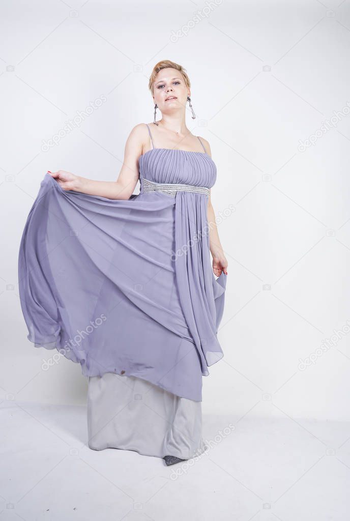 elegant thick female in a grey long dress. pretty plus size woman in evening dress standing on white studio background. short hair chubby girl in gray clothes posing alone.