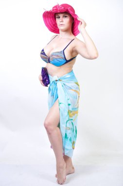 kıvrımlı rakam ile sevimli kız Studio beyaz arka plan üzerinde pareo ile fuşya pembe şapka ve mavi mayo duruyor. tek başına poz moda beachwear güzel kıvrımlı tombul kadın.
