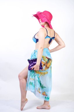 kıvrımlı rakam ile sevimli kız Studio beyaz arka plan üzerinde pareo ile fuşya pembe şapka ve mavi mayo duruyor. tek başına poz moda beachwear güzel kıvrımlı tombul kadın.