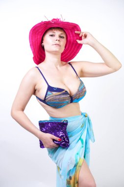 kıvrımlı rakam ile sevimli kız Studio beyaz arka plan üzerinde pareo ile fuşya pembe şapka ve mavi mayo duruyor. tek başına poz moda beachwear güzel kıvrımlı tombul kadın.
