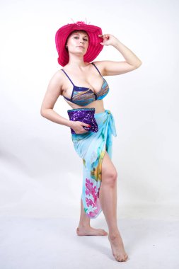 kıvrımlı rakam ile sevimli kız Studio beyaz arka plan üzerinde pareo ile fuşya pembe şapka ve mavi mayo duruyor. tek başına poz moda beachwear güzel kıvrımlı tombul kadın.