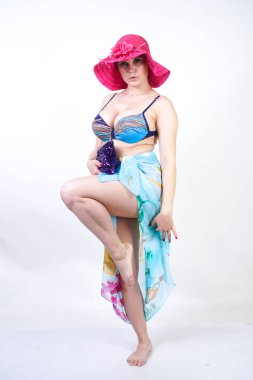 kıvrımlı rakam ile sevimli kız Studio beyaz arka plan üzerinde pareo ile fuşya pembe şapka ve mavi mayo duruyor. tek başına poz moda beachwear güzel kıvrımlı tombul kadın.