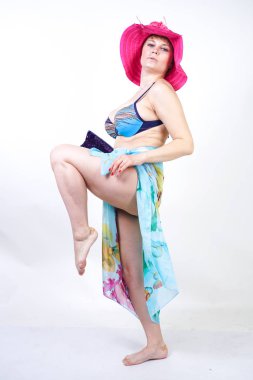 kıvrımlı rakam ile sevimli kız Studio beyaz arka plan üzerinde pareo ile fuşya pembe şapka ve mavi mayo duruyor. tek başına poz moda beachwear güzel kıvrımlı tombul kadın.