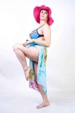 kıvrımlı rakam ile sevimli kız Studio beyaz arka plan üzerinde pareo ile fuşya pembe şapka ve mavi mayo duruyor. tek başına poz moda beachwear güzel kıvrımlı tombul kadın.