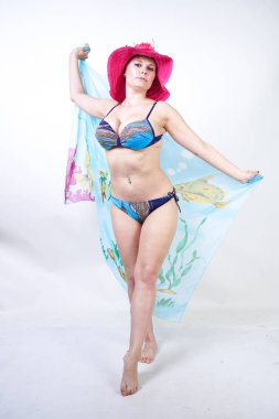 kıvrımlı rakam ile sevimli kız Studio beyaz arka plan üzerinde pareo ile fuşya pembe şapka ve mavi mayo duruyor. tek başına poz moda beachwear güzel kıvrımlı tombul kadın.