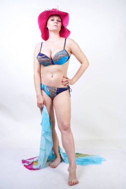 kıvrımlı rakam ile sevimli kız Studio beyaz arka plan üzerinde pareo ile fuşya pembe şapka ve mavi mayo duruyor. tek başına poz moda beachwear güzel kıvrımlı tombul kadın.