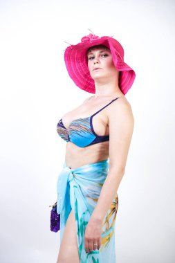 kıvrımlı rakam ile sevimli kız Studio beyaz arka plan üzerinde pareo ile fuşya pembe şapka ve mavi mayo duruyor. tek başına poz moda beachwear güzel kıvrımlı tombul kadın.