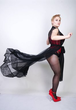 güzel şık artı kırmızı dantel korse kısa saçlı ve siyah sırf uzun bornoz ile sarışın, tek başına beyaz arka plan üzerinde poz çelik topuk ile dikiş ve kırmızı patent deri ayakkabı ile seksi külotlu çorap