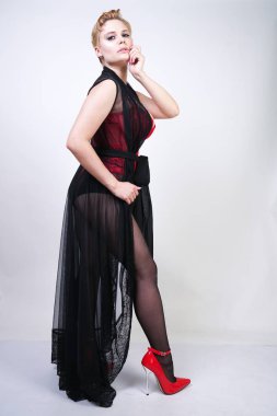 güzel şık artı kırmızı dantel korse kısa saçlı ve siyah sırf uzun bornoz ile sarışın, tek başına beyaz arka plan üzerinde poz çelik topuk ile dikiş ve kırmızı patent deri ayakkabı ile seksi külotlu çorap