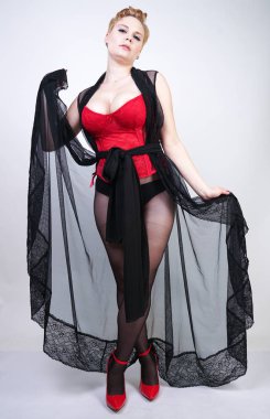 güzel şık artı kırmızı dantel korse kısa saçlı ve siyah sırf uzun bornoz ile sarışın, tek başına beyaz arka plan üzerinde poz çelik topuk ile dikiş ve kırmızı patent deri ayakkabı ile seksi külotlu çorap