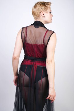 güzel şık artı kırmızı dantel korse kısa saçlı ve siyah sırf uzun bornoz ile sarışın, tek başına beyaz arka plan üzerinde poz çelik topuk ile dikiş ve kırmızı patent deri ayakkabı ile seksi külotlu çorap