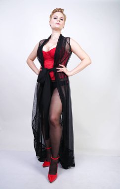 güzel şık artı kırmızı dantel korse kısa saçlı ve siyah sırf uzun bornoz ile sarışın, tek başına beyaz arka plan üzerinde poz çelik topuk ile dikiş ve kırmızı patent deri ayakkabı ile seksi külotlu çorap