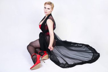 güzel şık artı kırmızı dantel korse kısa saçlı ve siyah sırf uzun bornoz ile sarışın, tek başına beyaz arka plan üzerinde poz çelik topuk ile dikiş ve kırmızı patent deri ayakkabı ile seksi külotlu çorap