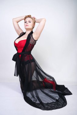 güzel şık artı kırmızı dantel korse kısa saçlı ve siyah sırf uzun bornoz ile sarışın, tek başına beyaz arka plan üzerinde poz çelik topuk ile dikiş ve kırmızı patent deri ayakkabı ile seksi külotlu çorap