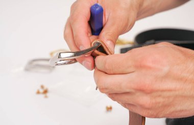 adam toka ile elleri deri kemer yapar. el yapımı hobi. genç adam onun tasarımcı kemerleri imalatı ile istirahat. elinde bir tornavida ile adam beyaz stüdyo arka plan üzerinde yakın perçin bükümler.