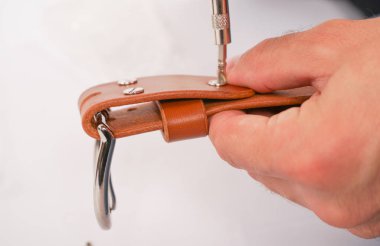 adam toka ile elleri deri kemer yapar. el yapımı hobi. genç adam onun tasarımcı kemerleri imalatı ile istirahat. elinde bir tornavida ile adam beyaz stüdyo arka plan üzerinde yakın perçin bükümler.