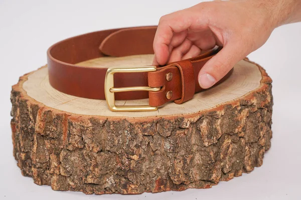 man makes by hands leather belt with buckle. handmade hobby. young man resting by manufacture his designer belts. man with a screwdriver in his hands twists rivets close up on white studio background.