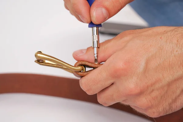 man makes by hands leather belt with buckle. handmade hobby. young man resting by manufacture his designer belts. man with a screwdriver in his hands twists rivets close up on white studio background.