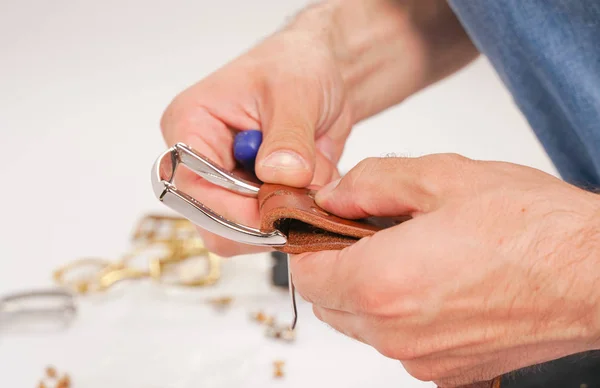 man makes by hands leather belt with buckle. handmade hobby. young man resting by manufacture his designer belts. man with a screwdriver in his hands twists rivets close up on white studio background.