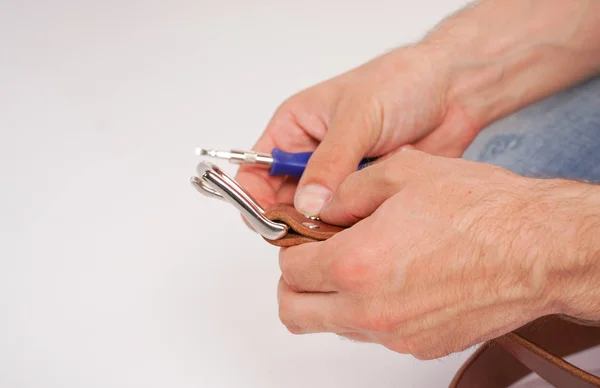 man makes by hands leather belt with buckle. handmade hobby. young man resting by manufacture his designer belts. man with a screwdriver in his hands twists rivets close up on white studio background.