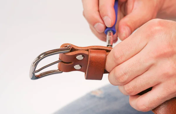 man makes by hands leather belt with buckle. handmade hobby. young man resting by manufacture his designer belts. man with a screwdriver in his hands twists rivets close up on white studio background.