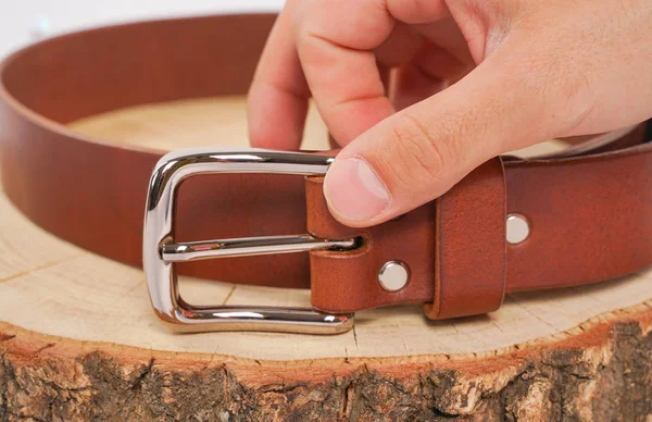 man makes by hands leather belt with buckle. handmade hobby. young man resting by manufacture his designer belts. man with a screwdriver in his hands twists rivets close up on white studio background.