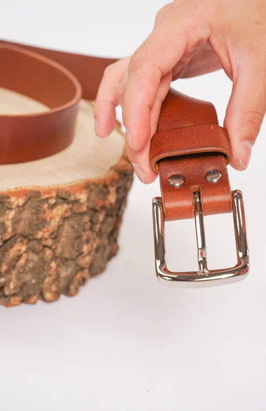 man makes by hands leather belt with buckle. handmade hobby. young man resting by manufacture his designer belts. man with a screwdriver in his hands twists rivets close up on white studio background.