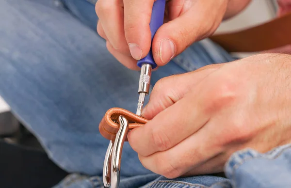 man makes by hands leather belt with buckle. handmade hobby. young man resting by manufacture his designer belts. man with a screwdriver in his hands twists rivets close up on white studio background.