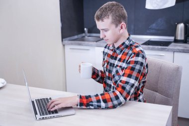 sevimli genç adam bir dizüstü bilgisayar ile ekose gömlek oturan ve çalışma, evde tek başına eğitim