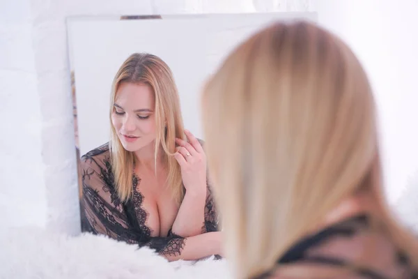 Encantador plus size mulher loira caucasiana vestida com belo rendas lingerie preta e olhando para si mesma no espelho em casa sozinha — Fotografia de Stock