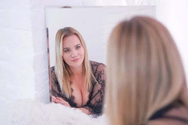 Charmig plus size kaukasiska blond kvinna klädd i vackra spetsar svarta underkläder och titta på sig själv i spegeln hemma ensam — Stockfoto