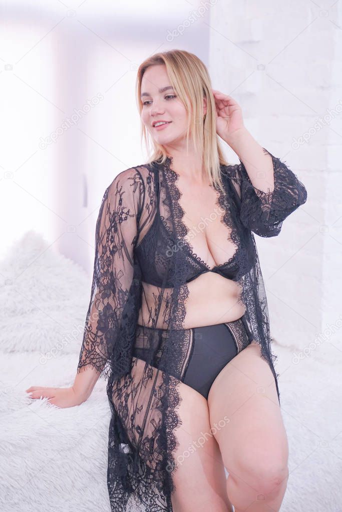 charming plus size caucasian woman dressed in a beautiful lace black lingerie and a sheer robe. curvaceous young girl in fashion underwear at home alone.
