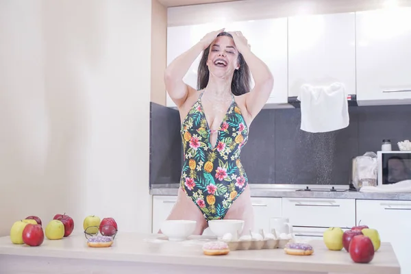 Mujer feliz en traje de baño de moda con hojas verdes posando en cocina blanca — Foto de Stock