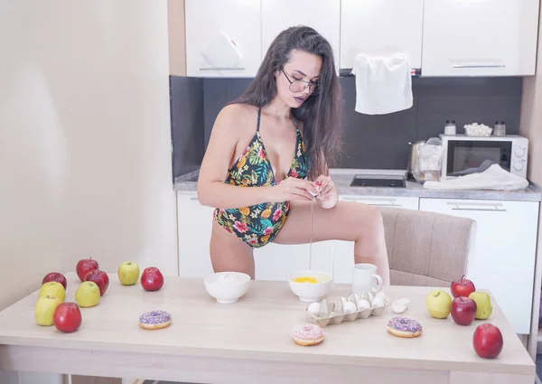 Щаслива жінка в модному купальнику з зеленим листям позує на білій кухні — стокове фото
