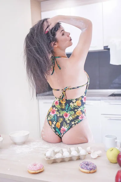 Happy woman in fashionable swimsuit with green leaves posing in white kitchen — Stock Photo, Image