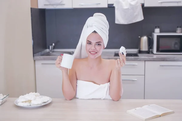 Young girl sitting in the kitchen after a shower wrapped in a white towel and resting — Stockfoto