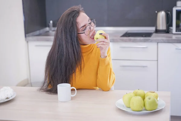 Крупним планом портрет прекрасної красивої дівчини, яка кусає яблуко на білому фоні кухні — стокове фото