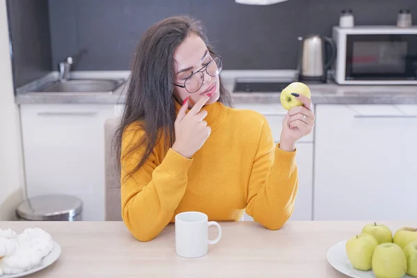 Крупным планом портрет красивой девушки, кусающей яблоко на белом кухонном фоне — стоковое фото