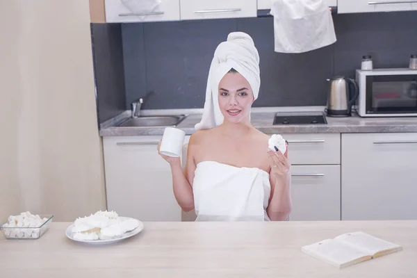 Young girl sitting in the kitchen after a shower wrapped in a white towel and resting — Stock Photo, Image