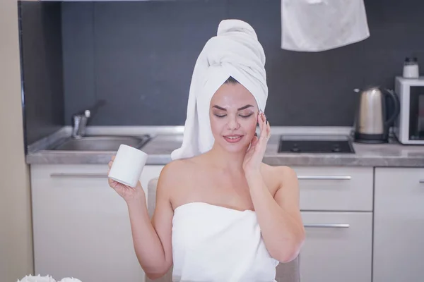 Young girl sitting in the kitchen after a shower wrapped in a white towel and resting — Stockfoto